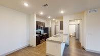 This well-appointed single-floor residence offers a clean, modern aesthetic with thoughtful design details throughout. The open-concept kitchen serves as a central hub, featuring dark espresso cabinetry, granite countertops, a light blue tile backsplash, and a full suite of stainless steel appliances including a refrigerator, electric range, and built-in microwave. A spacious kitchen island with a double sink and matching granite surface provides ample prep space and a natural gathering point that flows seamlessly into the adjacent living area. Wood-style luxury vinyl flooring runs throughout the main living spaces, adding warmth and cohesion to the layout. The living area is open and versatile, bathed in recessed lighting and offering a clean canvas for a variety of arrangements. Bedrooms are well-sized, each equipped with ceiling fans with light kits and windows fitted with blinds that allow for natural light control. Bathrooms are finished with granite vanity countertops and undermount sinks, with one full bath featuring a tiled tub-shower combination with a curved shower rod. A dedicated laundry area with shelving is also present within the unit. Throughout, the space maintains a bright, neutral palette that enhances its modern, move-in-ready appeal.
