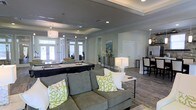 Located at 3202 W Nine Mile Rd. in Pensacola, Florida, this single-floor space offers a well-appointed, open-concept layout designed for both comfort and recreation. The main gathering area is anchored by a plush sectional sofa accented with vibrant throw pillows, creating an inviting lounge environment. A full-sized billiards table takes center stage nearby, making the space ideal for social gatherings and leisure activities. The interior features rich wood-look flooring that runs throughout, complemented by soft gray walls and crisp white crown molding that lend a clean, contemporary aesthetic. Tray ceilings with recessed lighting add architectural depth and a refined touch to the space, while pendant lighting provides warm, focused illumination over key areas. Large glass doors along one wall flood the interior with natural light and offer views to an outdoor area beyond, enhancing the overall sense of openness. A kitchenette or bar area is visible toward one end of the space, equipped for convenience and entertaining. The cohesive design, combining modern furnishings with thoughtful architectural details, creates a welcoming and versatile environment suitable for a variety of community or recreational uses.