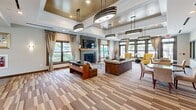 Located at 3600 Corriere Road in Easton, Pennsylvania, the Palmer View clubhouse is a thoughtfully designed community space spanning a generous single floor. Guests are welcomed through a polished entrance lobby featuring a dramatic tiled fireplace wall, a coffered ceiling with a statement chandelier, and bold accent colors that set an inviting tone.

The main living area impresses with soaring ceilings, floor-to-ceiling multi-pane windows dressed in sheer draping curtains, and an abundance of natural light. A built-in shelving unit with integrated workstations makes this space equally suited for relaxation and productivity. Adjacent seating areas offer a cozy fireplace and vibrant accent chairs for casual gatherings.

The dining area features elegant round tables with upholstered seating, set atop richly striped carpeting beneath a raised tray ceiling with recessed lighting. Wall sconces and framed artwork add a refined touch throughout.

The kitchen is equipped with granite countertops, a tile backsplash, stainless steel appliances including a full-size refrigerator and built-in microwave, and wood-toned cabinetry — all complemented by large windows overlooking the exterior.

A dedicated billiards room with wood-look tile flooring, exposed beam ceiling details, and a classic pool table rounds out the entertainment offerings. Warm wood trim and neutral tones unify the space throughout, creating a cohesive and welcoming community environment.