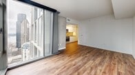 Located at 707 Terry Ave North in Seattle's First Hill neighborhood, this modern studio offers a thoughtfully designed single-floor layout comprising a living room, kitchen, bathroom, laundry, closet, and hallway. Warm wood-look flooring runs throughout, providing continuity and a welcoming feel across the entire space.

The living area is the standout feature of the unit, boasting expansive floor-to-ceiling glass windows and a sliding glass door that floods the room with natural light and frames views of the surrounding urban streetscape. Exposed concrete accent columns add an industrial architectural character that contrasts elegantly with the clean white walls.

The kitchen is efficiently designed with flat-front white cabinetry extending to the ceiling for ample storage, stainless steel appliances including a refrigerator, electric range, oven, and over-the-range microwave, as well as a tile backsplash and track lighting overhead.

A long, well-lit hallway connects the main living areas to the bathroom, in-unit laundry, and closet, keeping utility functions neatly separated. The recessed lighting throughout the hallway and living areas ensures a bright, clean ambiance. The overall design reflects a contemporary urban aesthetic, combining functional efficiency with modern finishes well-suited to city living in Seattle.
