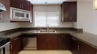 This two-story residence is designed with a practical and cohesive aesthetic throughout. The kitchen is a standout space, outfitted with rich dark-wood cabinetry extending to the ceiling, granite countertops, and a full suite of stainless steel appliances including a gas range, refrigerator, built-in microwave, and dishwasher. Large porcelain tile flooring and a window above the double basin sink bring in natural light, creating a clean and functional workspace. Pendant lighting adds a polished finishing touch.

The living and dining areas feature neutral-toned carpet and a sliding glass door that opens to a private balcony, allowing natural light to fill the space. A pendant light fixture anchors the dining area. The bedroom is generously sized with soft carpeting and a window overlooking the exterior.

Two bathrooms maintain the design consistency of the home, each featuring dark-wood vanities with granite countertops. The full bath includes a soaking tub with subway tile surround and a curved shower rod, while the second bath offers a clean, tile-floored layout. A dedicated in-unit stacked washer and dryer is conveniently accessible on each floor, adding notable practicality to everyday living.