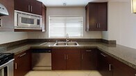 This two-story residence is designed with a practical and cohesive aesthetic throughout. The kitchen is a standout space, outfitted with rich dark-wood cabinetry extending to the ceiling, granite countertops, and a full suite of stainless steel appliances including a gas range, refrigerator, built-in microwave, and dishwasher. Large porcelain tile flooring and a window above the double basin sink bring in natural light, creating a clean and functional workspace. Pendant lighting adds a polished finishing touch.

The living and dining areas feature neutral-toned carpet and a sliding glass door that opens to a private balcony, allowing natural light to fill the space. A pendant light fixture anchors the dining area. The bedroom is generously sized with soft carpeting and a window overlooking the exterior.

Two bathrooms maintain the design consistency of the home, each featuring dark-wood vanities with granite countertops. The full bath includes a soaking tub with subway tile surround and a curved shower rod, while the second bath offers a clean, tile-floored layout. A dedicated in-unit stacked washer and dryer is conveniently accessible on each floor, adding notable practicality to everyday living.