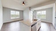 Located on Founder's Lane in Lebanon, Ohio, this well-appointed single-floor residence offers two bedrooms and two bathrooms with a thoughtfully designed open-concept layout. The combined kitchen and living area serves as the heart of the home, showcasing wood-look plank flooring, recessed lighting, and abundant natural light from large windows with views of the surrounding greenery. The kitchen is a standout feature, equipped with white shaker cabinetry, granite countertops, a center island with an undermount sink, and a full suite of stainless steel appliances including a refrigerator, range, and built-in microwave. Both bedrooms are carpeted for comfort, with large windows that invite natural light and outdoor views. The primary bedroom offers a generous footprint and connects to a well-finished bathroom featuring white cabinetry, granite countertops, an undermount sink, and hardwood-style flooring. The second bathroom mirrors this refined aesthetic. A dedicated laundry room includes a full-size washer and dryer with overhead shelving for added storage. A closet provides additional organization space, while two hallways connect the layout efficiently. The overall palette of soft grays and crisp whites lends the space a clean, contemporary ambiance throughout.