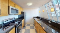 This two-story, one-bedroom, one-bathroom unit with a loft offers a distinctive urban living experience rooted in industrial-style architecture. The main level features warm hardwood flooring throughout the open living areas, complemented by crisp white walls that enhance the sense of light and space. Towering floor-to-ceiling grid-pane windows flood the interior with natural light while framing striking cityscape views, including a notable domed architectural landmark visible from the main living area. A metal ladder leads to the upper loft level, which provides additional flexible living or sleeping space with built-in closet storage and soaring ceiling heights.

The galley-style kitchen is well-appointed with warm maple cabinetry, dark granite countertops, stainless steel appliances including a refrigerator and over-the-range microwave, and a classic checkerboard-patterned tile floor. Pendant lighting above the counter adds a polished finishing touch.

The bathroom continues the quality finishes with a full tub-and-shower combination, maple vanity cabinetry, dark granite countertops, and a charming black-and-white mosaic tile floor. Additional storage is provided by a generous walk-in closet with built-in hanging rods, located off the bedroom area.