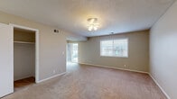 This single-floor residence offers four bedrooms, two bathrooms, and a practical, well-organized layout designed to maximize comfortable living. The main living area is open and generously sized, featuring soft neutral wall tones, plush wall-to-wall carpeting, a ceiling fan light fixture, and two windows — including a sliding glass door — that bring in natural light and outdoor views. The kitchen is efficiently designed with white cabinetry, dark stone-look countertops, tile flooring, and white appliances including a refrigerator, dishwasher, and range, all beneath a bright flush-mount ceiling light. The spacious primary bedroom is a standout feature, offering ample room, a ceiling fan, a large window, and a dedicated closet with built-in hanging rods. The additional bedrooms are well-proportioned, each with carpeted floors, neutral walls, and sliding or hinged closets with hanging storage. The two bathrooms are clean and functional: one features a full tub-shower combination with white tile surround and a wood-toned vanity, while the other includes a single-basin vanity with a large mirror. A connecting hallway ties the layout together, providing smooth flow between all areas of the home. Overall, the space presents a clean, neutral palette ideal for a variety of living arrangements.