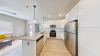 This well-designed single-floor residence offers a thoughtful layout with modern finishes throughout. The open-concept kitchen is a standout feature, showcasing crisp white shaker cabinetry, granite-look countertops, and a full suite of stainless steel appliances including a refrigerator, electric range, microwave, and dishwasher. A peninsula with an undermount sink and pendant lighting above creates a natural gathering point and provides additional prep space. White subway tile backsplash and light wood-look flooring complete the kitchen's clean, contemporary aesthetic. The living area flows seamlessly from the kitchen, benefiting from natural light through large windows with blinds and a ceiling fan overhead. A sliding door provides access to an outdoor balcony or patio, enhancing the connection to the exterior. The bedroom features plush carpeting, a bright window, and direct access to a well-appointed en-suite bathroom. The bathroom includes white cabinetry with granite-look countertops, and a walk-in closet is conveniently accessible from the same corridor. Light wood-look flooring carries consistently through the main living spaces, tying the home together with a warm, cohesive feel throughout.