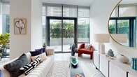Located in Miami's dynamic Edgewater neighborhood, this bright and contemporary 2-bedroom, 2-bathroom residence offers a thoughtfully designed single-level layout filled with natural light. The open-concept living, dining, and kitchen area forms the heart of the home, anchored by large floor-to-ceiling glass windows and sliding doors that connect seamlessly to a generous wraparound balcony. The outdoor space is framed by manicured tropical landscaping, including palm trees and lush hedging, creating a private urban retreat. The modern kitchen is outfitted with sleek dark cabinetry, stainless steel appliances, a tiled backsplash, and a white waterfall island with bar seating, all accented by stylish pendant lighting. Light-toned tile flooring flows throughout the entire residence, enhancing its clean, airy aesthetic. The primary bedroom is a well-proportioned suite featuring floor-to-ceiling windows with outdoor views and direct balcony access. The second bedroom also benefits from generous glazing and soaring ceilings with an architectural arched window detail. Both bathrooms are finished in a crisp, minimalist style with white cabinetry and framed mirrors. Additional highlights include a dedicated laundry closet with a stacked washer and dryer, multiple storage closets, and a welcoming entrance hallway.