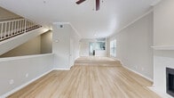 This three-floor home offers a thoughtfully designed layout with a blend of light hardwood flooring and plush carpeting throughout. The main living area features a distinctive split-level design, with light hardwood floors connecting the lower lounge space to a raised area leading into the kitchen. A classic white-mantled fireplace with marble surround serves as a focal point in the living room, complemented by crown molding and a ceiling fan overhead. Natural light filters through slatted blinds across multiple windows, creating a bright and airy atmosphere. The kitchen is equipped with stainless steel appliances and light countertops, while a dedicated in-unit laundry closet with a full washer and dryer set adds everyday convenience. Carpeted bedrooms are generously sized, each featuring ceiling fans and windows with outdoor views. A spacious walk-in closet with wire shelving provides ample storage. The bathroom is finished with large-format marble-look tile surrounding the soaking tub and shower, paired with gray cabinetry and white countertops. Carpeted stairs with white railings connect all three levels, completing this well-appointed multi-story home.