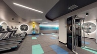 Located at 701 5th Avenue North in Seattle, WA, this contemporary fitness center offers a well-appointed, single-floor layout designed to support a full range of workout routines. The space features a striking design aesthetic, with a sweeping dark ceiling canopy that contrasts against crisp white walls, creating a sleek and energizing atmosphere throughout.

The cardio zone houses a row of treadmills and an elliptical trainer, each positioned in front of large, backlit circular mirrors that add both depth and a modern design element to the room. Adjacent to this area, the strength training section is equipped with a cable machine, a power rack with bench, and a full dumbbell rack, providing ample options for resistance training.

A dedicated open-floor stretching and functional training area features rubber flooring accented with teal and blue tiles, yoga mats, stability balls, resistance tools, and a balance trainer. A dramatic large-format mountain landscape mural spans an entire wall of this zone, adding a calming, nature-inspired focal point. Linear LED lighting runs across the ceiling, providing even, modern illumination throughout.

Built-in shelving, a restroom or shower enclosure, and organized storage areas round out the practical amenities of this thoughtfully designed fitness facility.