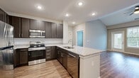 Located at 2183 S Withers Rd in Liberty, Missouri, this thoughtfully designed one-bedroom, one-bathroom residence offers a comfortable and modern living experience across a single floor. The open-concept kitchen and living area serves as the heart of the home, showcasing rich dark espresso cabinetry, granite countertops, a peninsula with a built-in sink, and a full suite of stainless steel appliances including a refrigerator, range, microwave, and dishwasher. Warm wood-look luxury vinyl plank flooring flows throughout the main living spaces, complementing the neutral wall tones and recessed lighting overhead. The living room benefits from vaulted ceilings, a ceiling fan, and a door leading to an outdoor space, allowing natural light to fill the room. The spacious bedroom features plush carpet, a ceiling fan, and large windows that bring in abundant natural light and outdoor views. The bathroom is outfitted with wood-look flooring, a tiled tub-shower combination, granite-topped vanity, and direct access to a generously sized walk-in closet complete with wire shelving and carpeted flooring. The overall ambiance is clean, modern, and move-in ready.