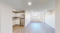 This single-floor unit offers a clean, contemporary design throughout, characterized by a neutral color palette, recessed lighting, and light-toned luxury vinyl plank flooring in the main living areas. The open-concept layout connects the kitchen and living space seamlessly, creating a generous, airy feel.

The kitchen is well-appointed with white flat-panel cabinetry extending to the ceiling, marble-style quartz countertops, a hexagonal tile backsplash, and a full suite of stainless steel appliances including a range, built-in microwave, dishwasher, and refrigerator. A stainless steel sink is positioned beneath additional cabinetry, maximizing storage throughout.

The living area is bright and open, with a large window framing views of surrounding trees, allowing abundant natural light to fill the space. The entryway features the same vinyl plank flooring and recessed lighting, providing a clean transition into the unit.

Bedrooms are carpeted for comfort and include windows with leafy outdoor views and recessed lighting. The bathroom is finished with large-format tile surrounds, a soaking tub with shower, hexagonal floor tile, a white vanity, and a well-lit mirror — all presented in a crisp, neutral palette.