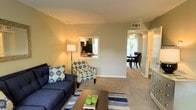 This two-story residence offers a thoughtfully designed layout that balances comfort and functionality. The main living area is carpeted and generously proportioned, providing ample room for seating and relaxation. Neutral-toned walls create a bright, welcoming atmosphere that complements a variety of interior styles. A distinctive pass-through window connects the living room to the kitchen, enhancing the open feel of the space while maintaining a sense of definition between the two areas. The kitchen, visible through the pass-through, features dark appliances and appears well-equipped for everyday use. Adjacent to the living room, the dining area benefits from natural light streaming in through a window, and is comfortably sized to accommodate a full dining set. A ceiling fan overhead adds both practicality and a finishing touch to the dining space. The flow between the living, dining, and kitchen areas makes the main floor ideal for both everyday living and entertaining. A hallway leads further into the home, hinting at additional rooms beyond. With two floors of living space, this residence offers room to spread out, making it a versatile and inviting home.