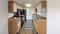 This single-story residence at Stonemill Village offers a well-organized layout designed for comfortable everyday living. The galley-style kitchen is efficiently arranged with cabinetry lining both sides, providing generous storage and counter space throughout. Dark granite-toned countertops contrast with the warm wood-accented cabinetry, while black appliances including a range, microwave, and refrigerator complete the functional setup. Wood-style flooring runs the length of the kitchen, and a window at the far end allows natural light to brighten the space.

The bedrooms feature neutral gray walls, plush carpeting, and windows fitted with blinds that invite outdoor views and natural light. The rooms offer versatile, open floor space suitable for a variety of furniture arrangements.

The living area is a standout feature, anchored by a tiled fireplace with a classic mantle that adds warmth and character to the room. Soft carpeting continues throughout, and large sliding glass doors open to an outdoor area, while an additional window ensures the space remains bright and connected to the outdoors. The overall layout, as seen in the floorplan view, reflects a practical and cohesive design that maximizes the use of available space across the single floor.