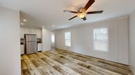 Located at 382 GA Highway 125 South in Tifton, Georgia, this single-story, 3-bedroom, 1-bathroom home offers a practical and updated layout within a peaceful, tree-lined community. The open-concept living, dining, and kitchen area forms the heart of the home, featuring warm wood-look plank flooring, crown molding, ceiling fans with lighting, and multiple windows that invite natural light throughout. The kitchen is well-appointed with crisp white shaker-style cabinetry, granite-look countertops, a stainless steel electric range, a double-basin sink, and a stainless steel refrigerator, making it both functional and visually clean. A hallway connects the main living area to the three bedrooms, each finished with the same wood-look flooring, neutral wall panels, and windows with blinds. The bedrooms each include closet access, with the primary bedroom offering a comfortable amount of private space. The full bathroom features a tub-shower combination with clean white surroundings and textured wall panels. Additional utility and laundry rooms provide practical storage and functionality. Outside, the home sits on an open lot within a multi-home community shaded by tall Georgia pines, with paved road access and a small deck entry.
