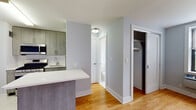 Located at 3 Davenport Ave in New Rochelle, NY, this single-floor unit offers a thoughtfully updated interior with a clean, contemporary aesthetic throughout. Warm honey-toned hardwood floors run through the main living areas, complementing the soft gray-blue walls that create a calm, neutral backdrop.

The open kitchen is outfitted with modern gray wood-grain cabinetry, a white quartz countertop, and a full suite of stainless steel appliances, including a gas range, over-the-range microwave, and bottom-freezer refrigerator. A peninsula counter extends into the living area, providing additional workspace and a natural division between the kitchen and the open living space.

The living area is generously proportioned, bright, and open, offering ample room for a variety of furniture arrangements. The bedroom features a large window with views of the surrounding neighborhood and waterway, filling the room with natural light. A closet with hanging storage is conveniently located nearby.

The bathroom has been finished to a high standard, with floor-to-ceiling marble-style tile, a wall-mounted white vanity with a black countertop and undermount sink, a large frameless glass sliding shower enclosure, and marble tile flooring. A window provides natural ventilation. Additional storage is available via a dedicated closet off the main hallway.