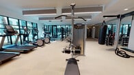Located at 1018 N Caldwell St in Charlotte, NC, this well-appointed fitness center delivers a complete workout experience within a thoughtfully designed, single-level facility. The space is bright and airy, benefiting from an abundance of natural light that streams through large, black-framed floor-to-ceiling windows, offering views of an outdoor pool area and surrounding greenery.

The main workout floor features a generous selection of Precor cardio equipment, including multiple treadmills, elliptical machines, and stair climbers, all arranged to maximize space and usability. A wall-mounted flat-screen TV accompanies the cardio zone for entertainment during workouts. Strength training is comprehensively covered with Precor cable machines, a leg press, a dedicated boxing station with a heavy bag, a power rack with battle ropes, free weights with a full dumbbell rack, and various functional training accessories.

A separate studio room, enclosed by sleek glass-panel partitions, houses cycling bikes, balance equipment, and open floor space for group or individual training. This room is distinguished by geometric gold pendant light fixtures and direct views of the pool. Acoustic panels suspended from the ceiling throughout the facility help manage sound, while light wood-look flooring and white walls contribute to the clean, modern aesthetic. The overall ambiance is energetic yet polished.
