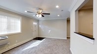 Located at 1 Brookwood Drive in Coram, New York, this single-floor home offers a thoughtfully arranged layout that maximizes both comfort and functionality. The floor plan reveals a spacious, open arrangement with distinct living zones connected by a central corridor, providing a natural flow throughout the interior.

The living areas are finished with plush wall-to-wall carpeting that adds warmth underfoot, while the central spaces feature tile or hard flooring, offering a practical contrast. Crown molding runs along the ceiling lines, lending an elegant, finished look to the rooms. Recessed lighting is installed throughout, providing even, ambient illumination, and ceiling fans in the main rooms enhance both comfort and air circulation.

The front entry door features decorative glass panels that invite natural light into the interior, brightening the space near the entryway. Neutral, soft-toned walls throughout create a clean, versatile backdrop well-suited to a variety of interior styles. Baseboard heating is present, ensuring comfort during colder months.

The central area of the home appears to serve as a transitional hub, connecting the various wings of the layout, which extend in a broad, open arrangement as seen from above. Overall, this home presents a well-maintained, move-in-ready interior with classic detailing and practical finishes.