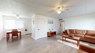 This single-story home offers a well-organized layout with multiple rooms suited for comfortable everyday living. The living area serves as the central gathering space, featuring light wood-look flooring, a ceiling fan with light fixture, and white panel walls that contribute to a bright, airy atmosphere. A large window allows natural light to fill the room, complemented by blinds for privacy. The space accommodates a seating arrangement anchored by a woven area rug, with a doorway leading further into the home.

The kitchen is efficiently designed with white cabinetry, granite-look countertops, a gas range, and a full-size refrigerator. A single-basin sink and under-cabinet ventilation hood add to the functional setup, while wood-look flooring continues throughout.

Multiple bedrooms are present, each featuring the same durable flooring, painted cinder block accent walls, and windows with blinds providing natural light. The rooms offer adequate space for standard bedroom furnishings.

The bathroom includes a full tub-shower combination with white surround, a toilet, and light-toned tile flooring, maintaining the clean, neutral aesthetic found throughout the home. Overall, the space presents a practical and cohesive interior.