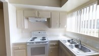 This two-story residence offers a practical and well-organized layout designed for comfortable everyday living. The kitchen is a standout functional space, featuring tile countertops, a white electric coil range with an overhead ventilation hood, and a double-basin stainless steel sink positioned beneath vertical blind-covered windows that allow ample natural light to fill the room. Cream-toned cabinetry lines both the upper and lower sections of the kitchen, providing generous storage throughout. The tile backsplash adds a clean, structured look to the cooking area, while the neutral color palette throughout creates a bright and airy atmosphere. The two-floor configuration of the home allows for a natural separation between living and private spaces, contributing to an organized and efficient flow. The overall design reflects a straightforward residential aesthetic with an emphasis on utility and livability, making it a well-suited space for everyday functionality.