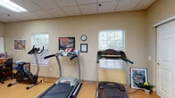 Located at 5863 Scioto Darby Rd in Hilliard, Ohio, this single-floor fitness facility offers a dedicated space for cardiovascular exercise and wellness. The workout area is outfitted with multiple treadmills and cardio machines, providing ample equipment for users to engage in their fitness routines. The room features a drop tile ceiling and warm, neutral-toned walls that create a clean and functional atmosphere. Natural light filters in through several windows fitted with horizontal blinds, offering pleasant views of the surrounding greenery and keeping the space feeling open and inviting. Light-toned flooring ties the room together, complementing the overall bright and practical aesthetic. Framed artwork and motivational décor, including an Ohio State University print, add a local character and personality to the space. A wall clock ensures users can easily track their workout time. The facility is well-maintained and thoughtfully arranged, making it a comfortable and accessible environment for regular exercise. Its straightforward, no-frills design prioritizes functionality while maintaining a welcoming ambiance suited for daily fitness use.
