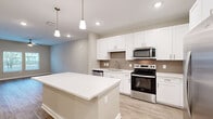 Located at Windsor Cay Blvd in Clermont, FL, this well-appointed single-floor residence offers a thoughtfully designed layout encompassing a kitchen, living room, bedroom, bathroom, utility room, and closet. The open-concept kitchen is a standout feature, showcasing crisp white shaker cabinetry, a neutral tile backsplash, and a full suite of stainless steel appliances including a French door refrigerator, electric range, built-in microwave, and dishwasher. A generously sized kitchen island with a white quartz countertop provides ample prep space and additional seating. Recessed lighting and pendant fixtures illuminate the kitchen, complementing the light wood-style luxury vinyl plank flooring that extends throughout the entire residence. The bedroom offers a comfortable footprint with dual windows that invite natural light and outdoor views, paired with a ceiling fan for year-round comfort. The bathroom features a full soaking tub and shower combination with floor-to-ceiling taupe tile surround. Neutral warm-toned walls throughout create a clean, contemporary ambiance, while the dedicated utility room and closet add practical storage solutions to this efficiently designed home.