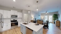 Located in Little River, SC, this well-appointed 2-bedroom, 2-bathroom single-story home offers a thoughtfully designed open-concept layout that seamlessly connects the kitchen, dining, and living areas. The kitchen is a standout feature, boasting white shaker cabinetry, a light blue island with a built-in sink and dishwasher, quartz countertops, stainless steel appliances including a refrigerator, range, microwave, and pendant lighting overhead. Light wood-tone flooring runs throughout the main living areas, adding warmth and continuity. The dining area offers generous space for entertaining, while the living room benefits from natural light and a ceiling fan. The primary bedroom is a comfortable retreat, featuring carpet flooring, a ceiling fan, and a walk-in closet with wire shelving. The second bedroom is equally well-sized and also includes closet storage. Both bathrooms are finished in clean, neutral tones; one features a full tub-shower combo with a white vanity. A dedicated laundry room houses full-size GE washer and dryer units with overhead wire shelving. The hallway connects all rooms efficiently, completing this practical and inviting single-floor home.
