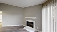 This well-appointed 2-bedroom, 2-bathroom single-floor unit offers a thoughtfully organized layout across a compact yet efficient footprint. The living room serves as the heart of the space, showcasing a white-framed fireplace with a clean mantel and sliding glass doors that invite natural light and provide outdoor access. Wood-look plank flooring in a warm gray tone extends throughout, complementing the neutral taupe wall palette and white trim. A textured ceiling adds subtle dimension to the open living area.

The galley-style kitchen features white cabinetry with light countertops, white appliances including a range and refrigerator, and track lighting overhead. Light-toned flooring and a practical layout make the space efficient for everyday use.

Both bedrooms are comfortably sized, with the primary bedroom offering a dedicated closet. Each room features the same durable wood-look flooring, neutral walls, and windows with horizontal blinds that allow for natural light. The two bathrooms are finished in a clean, white aesthetic — one includes a full tub-shower combination with tiled surround, and the other features a white vanity with storage cabinetry and a wall-mounted mirror. A hallway with two closets provides additional storage throughout the unit.