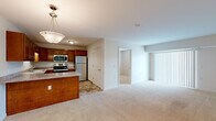 This single-floor, 2-bedroom, 1-bathroom unit offers a practical and efficiently designed layout. The open-concept kitchen flows directly into the living room, creating a connected and functional common area. The kitchen is well-appointed with warm medium-toned wood cabinetry, granite-style laminate countertops, and a full suite of stainless steel appliances including a range, microwave, refrigerator, and dishwasher. A peninsula with an overhang provides additional counter space and serves as a natural divider between the kitchen and the carpeted living area. The living room receives natural light through a sliding glass door fitted with vertical blinds.

Both bedrooms are carpeted and finished with neutral tones, offering a clean and versatile canvas. The primary bedroom includes a double-door closet with built-in wire shelving, providing organized storage. The second bedroom features a window with horizontal blinds for natural light and privacy.

The single bathroom is spacious and well-equipped, featuring stone-look tile flooring, a wood vanity with a sink and mirror, a glass-door shower, and accessibility grab bars. In-unit laundry connections are also located within or adjacent to the bathroom area, adding everyday convenience.