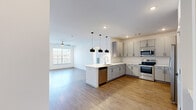 This well-appointed single-floor residence offers a thoughtfully designed layout encompassing three bedrooms, two bathrooms, and a dedicated laundry room. The open-concept kitchen and living area serves as the heart of the home, where light wood-style flooring flows seamlessly underfoot. The kitchen is outfitted with grey shaker-style cabinetry, a white quartz peninsula countertop, a white subway tile backsplash, and a full suite of stainless steel appliances including a range, microwave, dishwasher, and refrigerator. Stylish pendant lights hang above the peninsula, adding a contemporary touch. The adjoining living area benefits from natural light through large windows and features a ceiling fan overhead, with a door providing outdoor access. The three bedrooms are carpeted for comfort, each featuring ceiling fans and windows with exterior views. The primary bedroom offers a generously sized closet with built-in shelving and hanging rods. The bathrooms are finished with floating grey vanities, white quartz countertops, and wood-look tile flooring, with the primary bath showcasing a dual-sink vanity. A dedicated laundry room with a full-size washer and dryer completes this practical and modern home.