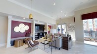 Located at 2170 Snyder Circle in Mount Pleasant, South Carolina, this single-floor community clubhouse offers a thoughtfully designed gathering space that blends contemporary style with comfortable functionality. The interior is anchored by a bold color palette of deep crimson and warm gold accents, contrasted against crisp white ceilings and light-toned large-format tile flooring that runs throughout the space.

The main lounge area is generously proportioned, featuring plush sectional and accent seating arranged around a central coffee table on a patterned area rug. Decorative gold pendant lights hang from the elevated ceiling, while recessed lighting provides even illumination throughout. A built-in shelving unit with an integrated flat-screen television serves as a media focal point, flanked by crimson accent walls adorned with decorative metallic disc arrangements.

Adjacent to the lounge, a bar-height communal workspace runs along a wall of expansive windows, offering abundant natural light and views of the surrounding community. Sleek pendant lights in cylindrical white and brass finishes cascade above the dark countertop, accompanied by upholstered bar-height chairs. A herringbone-tiled accent wall and a built-in beverage station complete this functional zone.

Large glass doors and generous windows throughout invite natural light and provide a seamless visual connection to the outdoors, giving the entire space an open, airy feel.