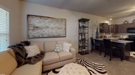 This single-floor residence offers a thoughtfully designed layout that balances comfort and functionality throughout its key living areas. The kitchen is outfitted with rich, dark wood cabinetry, granite-style countertops, and a full suite of black appliances including a refrigerator, range, built-in microwave, and dishwasher. Dark hardwood-style flooring anchors the kitchen and extends into the adjacent hallway, where a dedicated in-unit laundry closet provides added convenience. The living room features plush carpeting, a ceiling fan, and a window with blinds that allows natural light to fill the space. It comfortably accommodates a seating area and entertainment setup, creating a relaxed, welcoming atmosphere. The primary bedroom is generously sized with soft carpeting, a ceiling fan, and a bright window overlooking the exterior. A second bedroom offers similar warmth and comfort, also with carpeting and a ceiling fan. The bathroom presents dark wood vanity cabinetry, a white countertop, a framed mirror with overhead lighting, and hardwood-style flooring. Throughout the residence, neutral tones, consistent finishes, and practical design choices come together to create a cohesive and livable environment suited for everyday comfort.