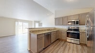 This single-story residence showcases a thoughtfully designed open-concept layout connecting the kitchen and living areas. The kitchen is a standout feature, equipped with stainless steel appliances including a range, dishwasher, microwave, and refrigerator. Warm-toned cabinetry pairs with granite-style countertops, and a peninsula with bar seating provides additional workspace and a natural division between the kitchen and the adjoining living area. Vaulted ceilings in the kitchen and main living space enhance the sense of openness, while wood-look luxury vinyl plank flooring runs throughout the common areas.

The living area is generously sized with neutral walls and access to natural light through a sliding glass door. Bedrooms are carpeted for comfort, with the primary bedroom offering two windows, a ceiling fan, and access to a spacious walk-in closet fitted with wire shelving systems. The bathroom features wood-look flooring, granite-topped vanity cabinetry, a walk-in shower, and coordinating fixtures. Additional bedrooms are well-proportioned with windows admitting natural light. Throughout, the home maintains a clean, neutral palette suited to a variety of furnishing styles.