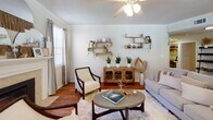 This single-floor residence offers a thoughtfully designed layout with warm, neutral tones and consistent hardwood flooring throughout the main living areas. The living room serves as a welcoming focal point, centered around a tile-surround fireplace with a classic white mantle, flanked by multiple windows that fill the space with natural light. Crown molding and a ceiling fan add traditional character to the room.

The dining area is defined by a pendant light fixture overhead and a large window with garden views, creating an intimate setting. The kitchen features white cabinetry with ample storage, light countertops, and hardwood flooring, providing a clean, functional workspace.

The primary bedroom is generously proportioned, with plush carpeting, a ceiling fan, and windows allowing natural light. A second bedroom also offers carpeted flooring and windows. Each bathroom includes a single-sink vanity with white cabinetry and a shower-tub combination. One bathroom features a long vanity with additional storage.

A dedicated in-unit laundry closet accommodates a full-sized washer and dryer with overhead shelving. Throughout, the residence maintains a cohesive, calm aesthetic with neutral walls and warm wood accents.