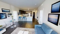 This single-floor residence showcases a thoughtfully designed open-concept layout that effortlessly connects the living and kitchen areas into one cohesive, flowing space. Rich, dark hardwood flooring runs throughout, providing a warm and grounding contrast to the bright white walls and light-toned ceilings above.

The kitchen is a standout feature, outfitted with dark espresso cabinetry, stainless steel appliances including a French door refrigerator, and a sleek white peninsula with bar seating for two. Recessed and pendant lighting illuminate the workspace, creating an inviting area for both cooking and casual dining.

The living area is generously proportioned, accommodating a large area rug, a comfortable sofa, and a glass accent table, all contributing to an airy yet intimate atmosphere. Clean white walls and recessed lighting throughout maintain a modern, uncluttered aesthetic.

Additional doors visible from the main living space suggest access to private bedrooms and bathrooms, hinting at a well-organized floor plan that balances open entertaining spaces with private retreats. The overall design reflects a contemporary sensibility, combining functional layouts with stylish finishes for comfortable everyday living.