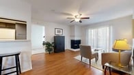 This single-floor residence offers a thoughtfully designed layout with a cohesive blend of hardwood-style flooring and neutral tones throughout. The living room serves as the heart of the home, anchored by a corner fireplace with a white surround and complemented by a ceiling fan with integrated lighting overhead. A textured ceiling adds subtle architectural character, while vertical blinds covering a large sliding door allow for adjustable natural light. Adjacent to the living room, a dedicated dining area features hardwood-style flooring and convenient pass-through access to the kitchen, making entertaining straightforward.

The galley-style kitchen is outfitted with dark cabinetry, white countertops, and white appliances including a range, dishwasher, and refrigerator, all set atop matching hardwood-style flooring. The bedrooms are carpeted for comfort, with one featuring multiple windows that fill the space with natural light and direct access to a spacious walk-in closet. An additional walk-in closet provides generous storage. The full bathroom includes a tiled tub-shower combination, hardwood-style flooring, and a vanity with a framed mirror and blue-gray cabinetry.