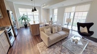 This contemporary single-floor residence offers a thoughtfully designed open-concept layout that seamlessly connects the kitchen, dining, and living areas. The kitchen is outfitted with sleek wood-grain cabinetry extending to the ceiling, stainless steel appliances including a gas range, dishwasher, and French door refrigerator, complemented by a subway tile backsplash and a breakfast bar island. Track lighting and pendant fixtures illuminate the space, while rich hardwood flooring flows throughout the main living area. The living room is bright and welcoming, featuring large windows and sliding glass doors that open to a balcony, flooding the space with natural light and providing outdoor views. The space includes multiple bedrooms, each carpeted and featuring large windows with outdoor views and built-in closet storage. The primary bedroom offers a serene, neutral color palette, while additional bedrooms provide versatile living options. Two bathrooms serve the residence — one featuring a wood-toned vanity, wide mirror, and a glass-enclosed walk-in shower, and the other offering a full bathtub and shower combination with clean white tile finishes. Throughout, the neutral tones, modern finishes, and abundant natural light create a cohesive and inviting living environment.