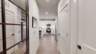 This single-floor residence offers a cohesive, modern design across two bedrooms, one bathroom, and a combined kitchen and living area, all finished with a consistent neutral palette and light-toned wood-look flooring throughout. A welcoming entry hallway leads directly toward the kitchen, which features floor-to-ceiling white shaker cabinetry with matte black hardware, white quartz countertops, a subway tile backsplash, and a full suite of stainless steel appliances including a range, over-the-range microwave, and refrigerator. The adjacent living room is bright and open, with recessed lighting and multiple windows that allow ample natural light, plus access to a private balcony overlooking the surrounding landscaped grounds. The primary bedroom is a comfortable, well-proportioned room with large windows and soft neutral tones. The second bedroom mirrors this calm aesthetic. Both bedrooms are supported by two dedicated closets, including a walk-in with wire shelving systems. The bathroom is finished with a white vanity, quartz countertop, a large black-framed mirror, matte black fixtures, and a glass-enclosed shower. Recessed lighting throughout maintains a clean, uniform ambiance.