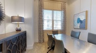 Located at 1680 Bluewater Way in Charleston, South Carolina, this single-floor space offers a refined and professionally designed environment with a cohesive, sophisticated aesthetic throughout. The interior showcases a neutral color palette anchored by crisp white walls, light-toned flooring with a subtle textured pattern, and carefully curated furnishings that balance style with functionality. A standout feature is the meeting or conference area, which is outfitted with a sleek, curved table and cushioned ergonomic chairs in muted grey tones — ideal for professional gatherings or focused work sessions. Large windows dressed with patterned semi-sheer curtains and wood-slat blinds allow natural light to filter softly into the space, creating a bright yet comfortable atmosphere. A dark navy credenza with decorative lattice-style hardware adds a bold contrast to the otherwise light interior, while framed artwork contributes to the polished, curated feel of the room. The overall ambiance is one of understated elegance — professional yet welcoming — making this space well-suited for business operations, client meetings, or administrative functions in the Charleston area.