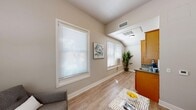 Located at 475–497 Marsh St in San Luis Obispo, California, this efficiently designed one-bedroom, one-bathroom unit offers a thoughtful layout across a single floor. The living area features light hardwood-style flooring, neutral walls, and multiple windows dressed with white blinds that invite ample natural light. An angled ceiling detail adds subtle architectural interest to the space. A kitchenette with warm wood cabinetry and a granite-look countertop with sink sits conveniently adjacent to the living area, maximizing functionality without sacrificing openness. The living room comfortably accommodates a seating arrangement and provides a welcoming atmosphere for everyday use. The bedroom is a cozy, well-proportioned retreat featuring the same hardwood-style flooring, a large double window for natural light, and a full-width louvered bi-fold closet offering practical storage. The bathroom is neatly appointed with a vanity, a tub/shower combination with a decorative curtain, grab bars for accessibility, and a stylish leaf-patterned mirror. Throughout the unit, the consistent use of soft gray tones, clean white trim, and warm wood accents creates a cohesive, calming aesthetic. This unit is ideally situated in the heart of San Luis Obispo, close to local amenities and the vibrant downtown area.