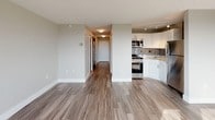 This thoughtfully designed studio in Cary offers a single-floor layout that makes efficient use of its space. The open-concept living area is anchored by warm hardwood-style flooring that extends throughout, creating a cohesive and inviting atmosphere. Large windows flood the main living space with abundant natural light while framing expansive views of the surrounding cityscape and skyline — a standout feature of the unit.

The kitchen is well-equipped and modern, showcasing granite countertops, crisp white cabinetry with brushed nickel hardware, a grey subway tile backsplash, and stainless steel appliances including a gas range, over-the-range microwave, and refrigerator. A stainless steel sink with a contemporary gooseneck faucet completes the space, making it both functional and stylish.

A hallway leads to the bathroom, which features a white vanity, wood-look tile flooring, and a glass-door standing shower with chrome fixtures. The neutral color palette throughout — soft whites and warm greys — lends the space a clean, modern aesthetic. Track lighting in the kitchen and recessed lighting in the bathroom add to the practical yet polished finish of this well-maintained studio.