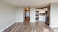 This thoughtfully designed studio in Cary offers a single-floor layout that makes efficient use of its space. The open-concept living area is anchored by warm hardwood-style flooring that extends throughout, creating a cohesive and inviting atmosphere. Large windows flood the main living space with abundant natural light while framing expansive views of the surrounding cityscape and skyline — a standout feature of the unit.

The kitchen is well-equipped and modern, showcasing granite countertops, crisp white cabinetry with brushed nickel hardware, a grey subway tile backsplash, and stainless steel appliances including a gas range, over-the-range microwave, and refrigerator. A stainless steel sink with a contemporary gooseneck faucet completes the space, making it both functional and stylish.

A hallway leads to the bathroom, which features a white vanity, wood-look tile flooring, and a glass-door standing shower with chrome fixtures. The neutral color palette throughout — soft whites and warm greys — lends the space a clean, modern aesthetic. Track lighting in the kitchen and recessed lighting in the bathroom add to the practical yet polished finish of this well-maintained studio.