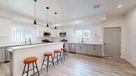 Located at 1360 West 35th Street in Los Angeles, this expansive four-floor property offers an impressive 17 bedrooms and 11 bathrooms, making it well-suited for large-group or multi-occupant living. The modern kitchen is a standout feature, boasting white shaker cabinetry, quartz countertops, stainless steel appliances — including a gas range, dishwasher, and dual refrigerators — and a central island with seating for several. Recessed lighting and sleek pendant fixtures illuminate the space, which is finished with light-toned hardwood-style flooring found throughout the property. The open living and dining area on the ground floor is bright and welcoming, with recessed lighting, a wall-mounted TV, seating, and direct access to the staircase connecting all four floors. Bedrooms are clean and minimalist, featuring white walls, natural light from multiple windows with neighborhood views, and the same consistent flooring. Bathrooms are finished in a crisp, all-white palette with walk-in showers, white vanities, and chrome fixtures. Two staircases provide convenient vertical circulation across all levels. The overall ambiance is clean, contemporary, and functional, with a cohesive modern aesthetic carried throughout every floor.