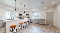 Located at 1360 West 35th Street in Los Angeles, this expansive four-floor property offers an impressive 17 bedrooms and 11 bathrooms, making it well-suited for large-group or multi-occupant living. The modern kitchen is a standout feature, boasting white shaker cabinetry, quartz countertops, stainless steel appliances — including a gas range, dishwasher, and dual refrigerators — and a central island with seating for several. Recessed lighting and sleek pendant fixtures illuminate the space, which is finished with light-toned hardwood-style flooring found throughout the property. The open living and dining area on the ground floor is bright and welcoming, with recessed lighting, a wall-mounted TV, seating, and direct access to the staircase connecting all four floors. Bedrooms are clean and minimalist, featuring white walls, natural light from multiple windows with neighborhood views, and the same consistent flooring. Bathrooms are finished in a crisp, all-white palette with walk-in showers, white vanities, and chrome fixtures. Two staircases provide convenient vertical circulation across all levels. The overall ambiance is clean, contemporary, and functional, with a cohesive modern aesthetic carried throughout every floor.