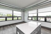 Located at 1261 Eighth Street in West Des Moines, Iowa, this thoughtfully designed two-bedroom, two-bathroom unit offers a clean, contemporary aesthetic across a single floor. The open-concept kitchen and living area serves as the heart of the home, featuring gray cabinetry, stainless steel appliances including a refrigerator, range, microwave, and dishwasher, and a central island with a white countertop. Expansive windows allow generous natural light to fill the space, offering views of the surrounding neighborhood. Exposed ductwork along the ceiling adds an industrial touch to the modern design. Wood-look plank flooring runs consistently throughout, complementing the crisp white walls and gray accent baseboards and door frames. Both bedrooms are comfortably sized, with the primary bedroom featuring direct access to its own bathroom. Each bathroom is outfitted with a vanity, modern cabinetry in coordinating tones, and either a tub or walk-in shower. A dedicated laundry area, multiple closets for ample storage, and a central hallway connecting all rooms round out the functional layout. The overall ambiance is bright, clean, and move-in ready.