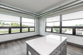 Located at 1261 Eighth Street in West Des Moines, Iowa, this thoughtfully designed two-bedroom, two-bathroom unit offers a clean, contemporary aesthetic across a single floor. The open-concept kitchen and living area serves as the heart of the home, featuring gray cabinetry, stainless steel appliances including a refrigerator, range, microwave, and dishwasher, and a central island with a white countertop. Expansive windows allow generous natural light to fill the space, offering views of the surrounding neighborhood. Exposed ductwork along the ceiling adds an industrial touch to the modern design. Wood-look plank flooring runs consistently throughout, complementing the crisp white walls and gray accent baseboards and door frames. Both bedrooms are comfortably sized, with the primary bedroom featuring direct access to its own bathroom. Each bathroom is outfitted with a vanity, modern cabinetry in coordinating tones, and either a tub or walk-in shower. A dedicated laundry area, multiple closets for ample storage, and a central hallway connecting all rooms round out the functional layout. The overall ambiance is bright, clean, and move-in ready.