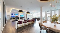 Located at 375 54th Ave N in Saint Petersburg, Florida, this impressive single-floor amenity space offers a diverse range of recreational and social areas designed to engage and entertain. The open-concept social lounge serves as the centerpiece, featuring floor-to-ceiling windows that flood the space with natural light and frame panoramic outdoor views. Plush navy blue seating, a shuffleboard table, and a stylish bar counter with velvet-upholstered stools create an inviting atmosphere for gathering. Large-format pendant lighting and cove-lit ceilings add a polished, modern aesthetic throughout.

A dedicated arcade room stands out with bold Pac-Man themed wallpaper, arcade cabinets, pinball machines, and tabletop gaming units, all set beneath a warm coffered ceiling. Adjacent to this is a golf simulator bay, outfitted with putting green turf, a projection screen, and comfortable lounge seating. A climbing wall enclosed in glass adds an active, sporty dimension to the space, while fitness equipment nearby supports wellness-focused use.

The space also includes a quieter lounge area with access to a furnished outdoor terrace, offering open-air seating with scenic waterfront vistas. Throughout, the design balances contemporary finishes with vibrant, themed accents, creating a dynamic and well-appointed environment.