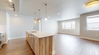 This thoughtfully designed single-floor residence offers a clean, contemporary aesthetic with an open-concept layout that seamlessly connects the kitchen and living area. The kitchen is a standout feature, anchored by a large island with a white quartz countertop, an undermount sink, and a warm wood-grain cabinet finish. A suite of stainless steel appliances — including a French door refrigerator, range, and microwave — is complemented by light wood cabinetry with track lighting overhead. Pendant lights hang above the island, adding a stylish focal point. The adjacent living area is bright and open, benefiting from natural light through a large window. Durable wood-look flooring runs throughout the main living spaces, while bedrooms feature plush neutral carpeting. Each bedroom offers a comfortable, well-proportioned space with windows that invite natural light. The primary bathroom includes a single-sink vanity with quartz countertop, wood-tone cabinetry, a full tub-shower combination, and large-format tile flooring. A second bathroom provides a dual-sink vanity with matching finishes. A dedicated walk-in closet features built-in shelving and hanging rods, offering generous storage. The in-unit laundry room houses a full-size front-loading washer and dryer with additional shelving above.