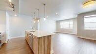 This thoughtfully designed single-floor residence offers a clean, contemporary aesthetic with an open-concept layout that seamlessly connects the kitchen and living area. The kitchen is a standout feature, anchored by a large island with a white quartz countertop, an undermount sink, and a warm wood-grain cabinet finish. A suite of stainless steel appliances — including a French door refrigerator, range, and microwave — is complemented by light wood cabinetry with track lighting overhead. Pendant lights hang above the island, adding a stylish focal point. The adjacent living area is bright and open, benefiting from natural light through a large window. Durable wood-look flooring runs throughout the main living spaces, while bedrooms feature plush neutral carpeting. Each bedroom offers a comfortable, well-proportioned space with windows that invite natural light. The primary bathroom includes a single-sink vanity with quartz countertop, wood-tone cabinetry, a full tub-shower combination, and large-format tile flooring. A second bathroom provides a dual-sink vanity with matching finishes. A dedicated walk-in closet features built-in shelving and hanging rods, offering generous storage. The in-unit laundry room houses a full-size front-loading washer and dryer with additional shelving above.