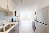 Located in Atlanta's vibrant Old Fourth Ward neighborhood, this contemporary unit at 299 N Highland Ave offers a thoughtfully designed open-concept layout. The kitchen and living area flow seamlessly together, creating a bright, airy atmosphere enhanced by large windows that invite abundant natural light. The kitchen features sleek two-tone cabinetry in white and warm wood tones, light quartz countertops, a classic subway tile backsplash, and stainless steel appliances, including a refrigerator, electric range, and built-in microwave. Light wood-look flooring runs throughout the main living area, reinforcing the clean, modern aesthetic. The living space is open and versatile, with a neutral color palette and large windows offering views of the surrounding neighborhood. The full bathroom is finished with large-format ceramic tile flooring, a soaking tub with tiled surround, a modern vanity with quartz countertop, and warm wood cabinetry. A dedicated laundry area features a stacked washer and dryer unit alongside built-in wire shelving, providing practical storage. The unit's contemporary design, quality finishes, and convenient location near the BeltLine and Ponce City Market make it a well-appointed urban residence.