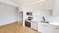 Located at 517 N Shipley Street in Wilmington, Delaware, this contemporary single-floor residence showcases a clean, modern aesthetic defined by crisp white finishes, light hardwood flooring, and matte black hardware accents throughout. The open-concept kitchen is a functional centerpiece, equipped with full-height white cabinetry that maximizes vertical storage, stainless steel appliances including a range, microwave, and dishwasher, and a sleek white quartz countertop with an undermount sink featuring a matte black faucet. Large floor-to-ceiling windows flood the kitchen and living area with abundant natural light while offering expansive views of the surrounding Wilmington cityscape. A long, well-lit corridor connects the living spaces to the private areas of the home, lined with built-in storage and recessed ceiling lighting that maintains a bright, airy atmosphere. Bedrooms are outfitted with sliding panel closets and warm hardwood floors, providing a calm and organized retreat. The bathroom is elegantly appointed with large-format warm beige floor tiles, a frameless glass-enclosed walk-in shower with full-height tile surround, a wall-mounted floating vanity with ample drawer storage, and continued matte black fixture detailing. The overall design balances minimalist style with practical functionality, creating a cohesive and inviting living environment.